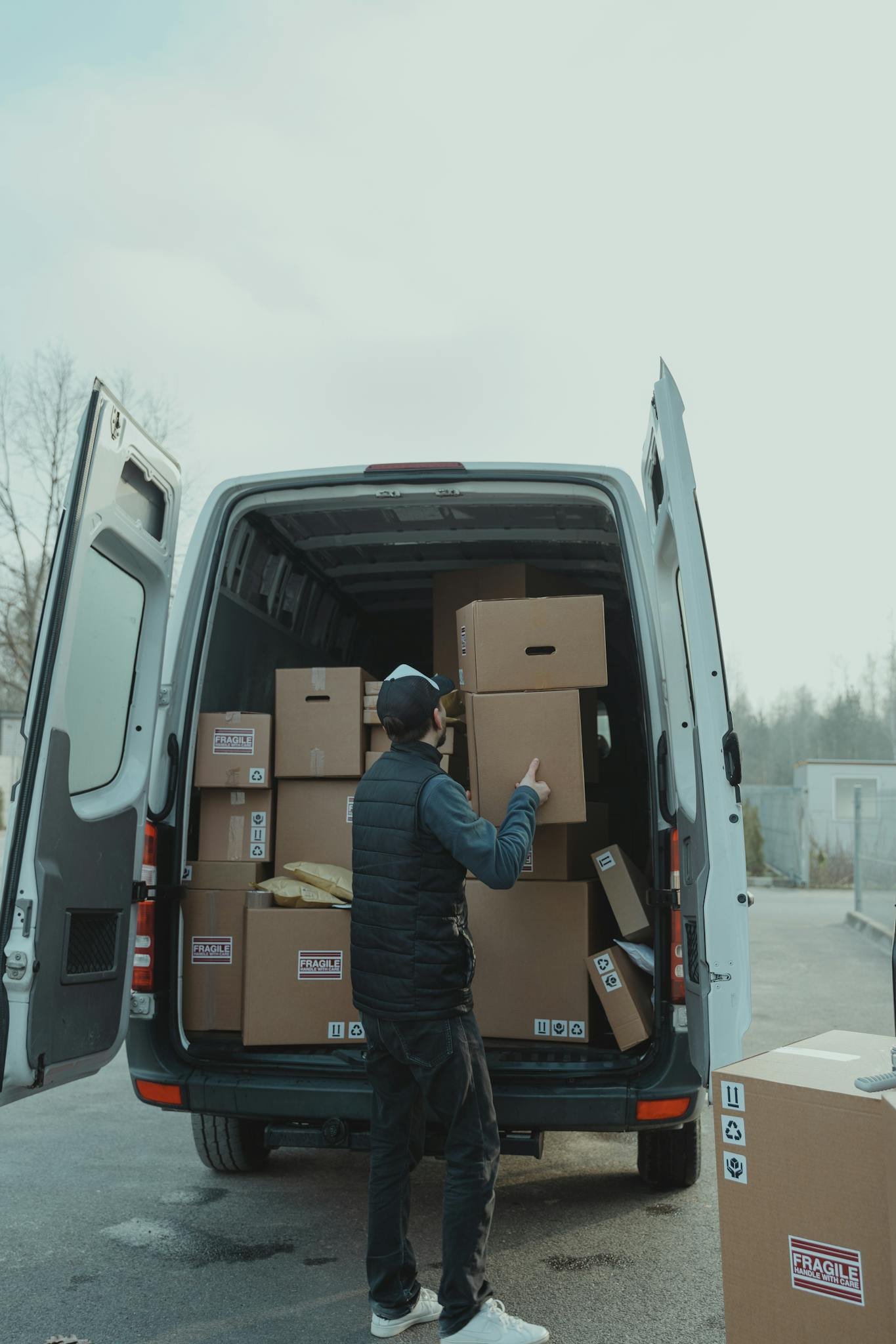 A delivery worker loading cardboard boxes into a van, preparing for shipment outdoors.