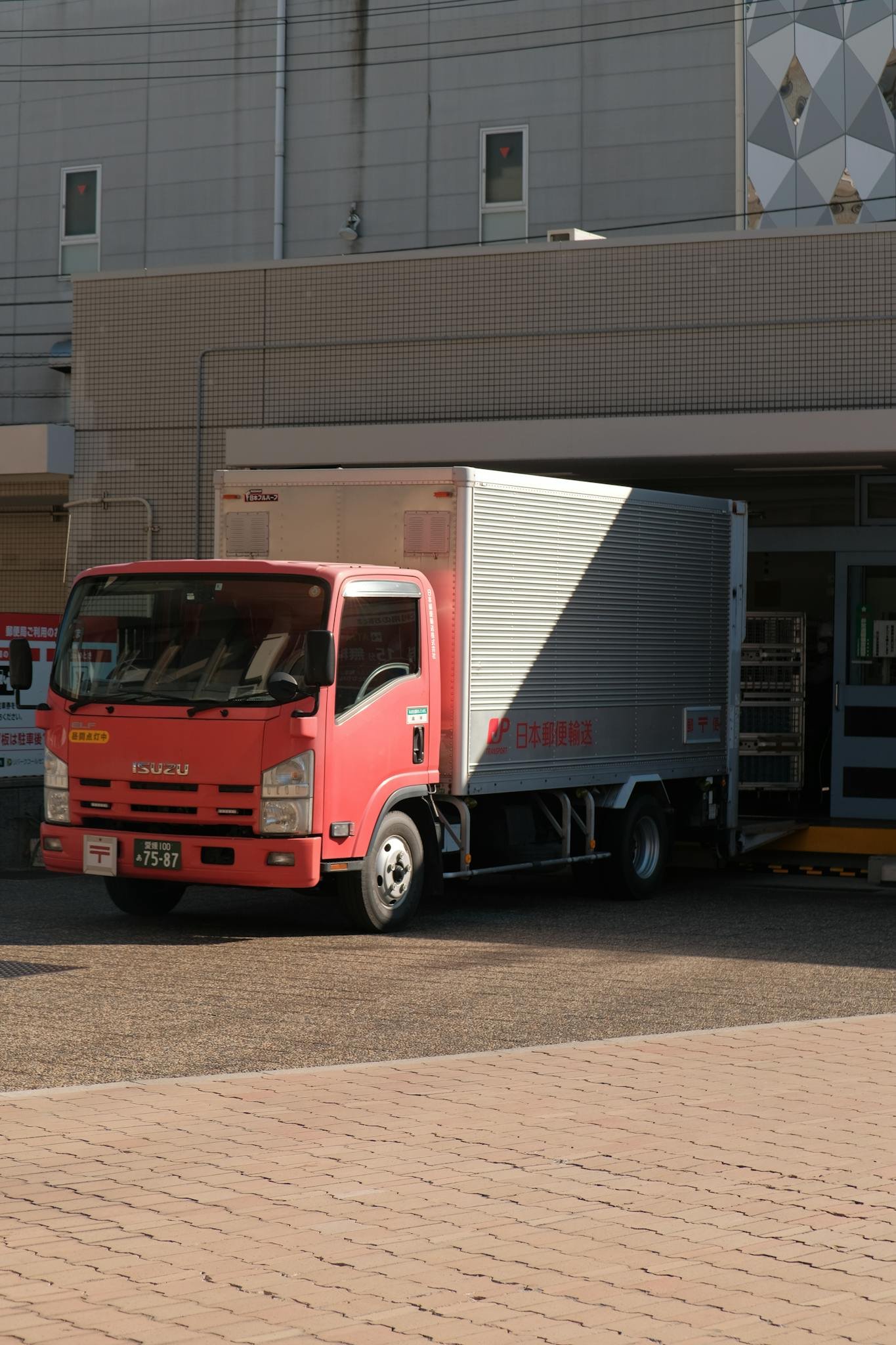A red delivery truck unloading goods at a warehouse on a sunny day in the city.